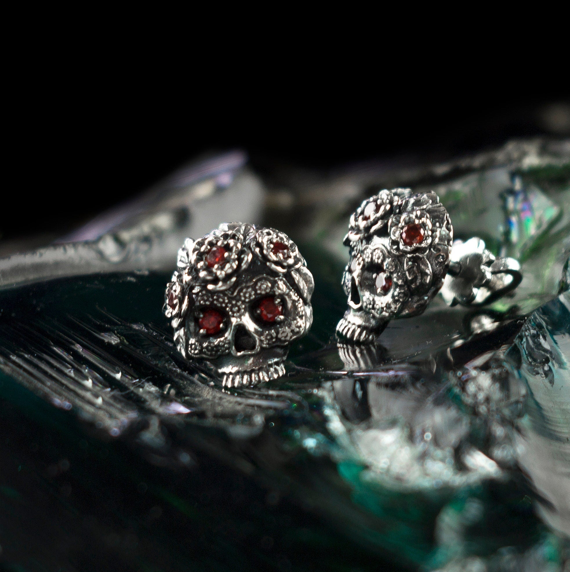 Frida floral skull stud earrings with red CZ eyes on green glass, angled