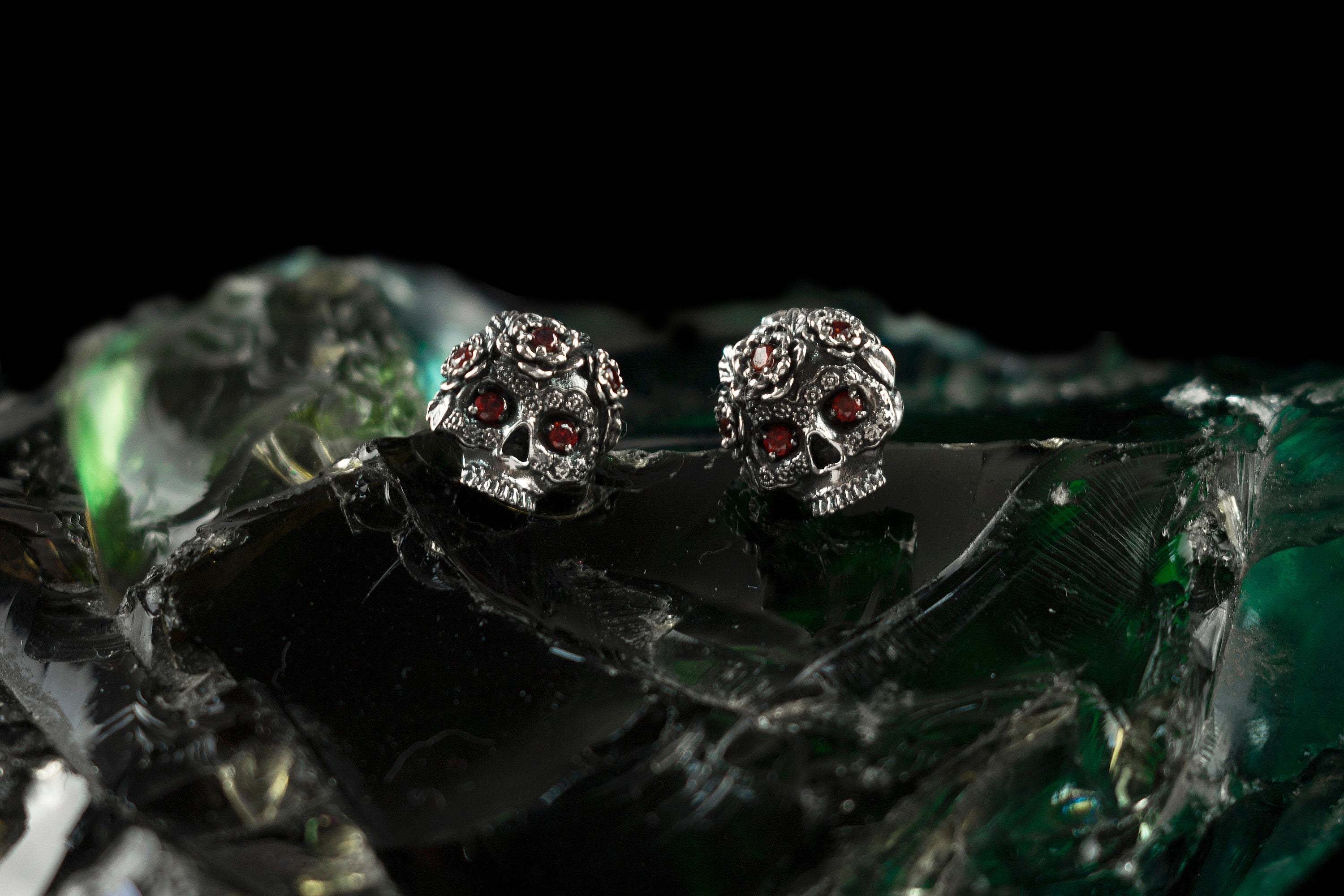 Frida skull stud earrings with red stones on green glass, wide view