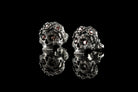 Pair of Frida skull stud earrings with red CZ and reflection, angled view