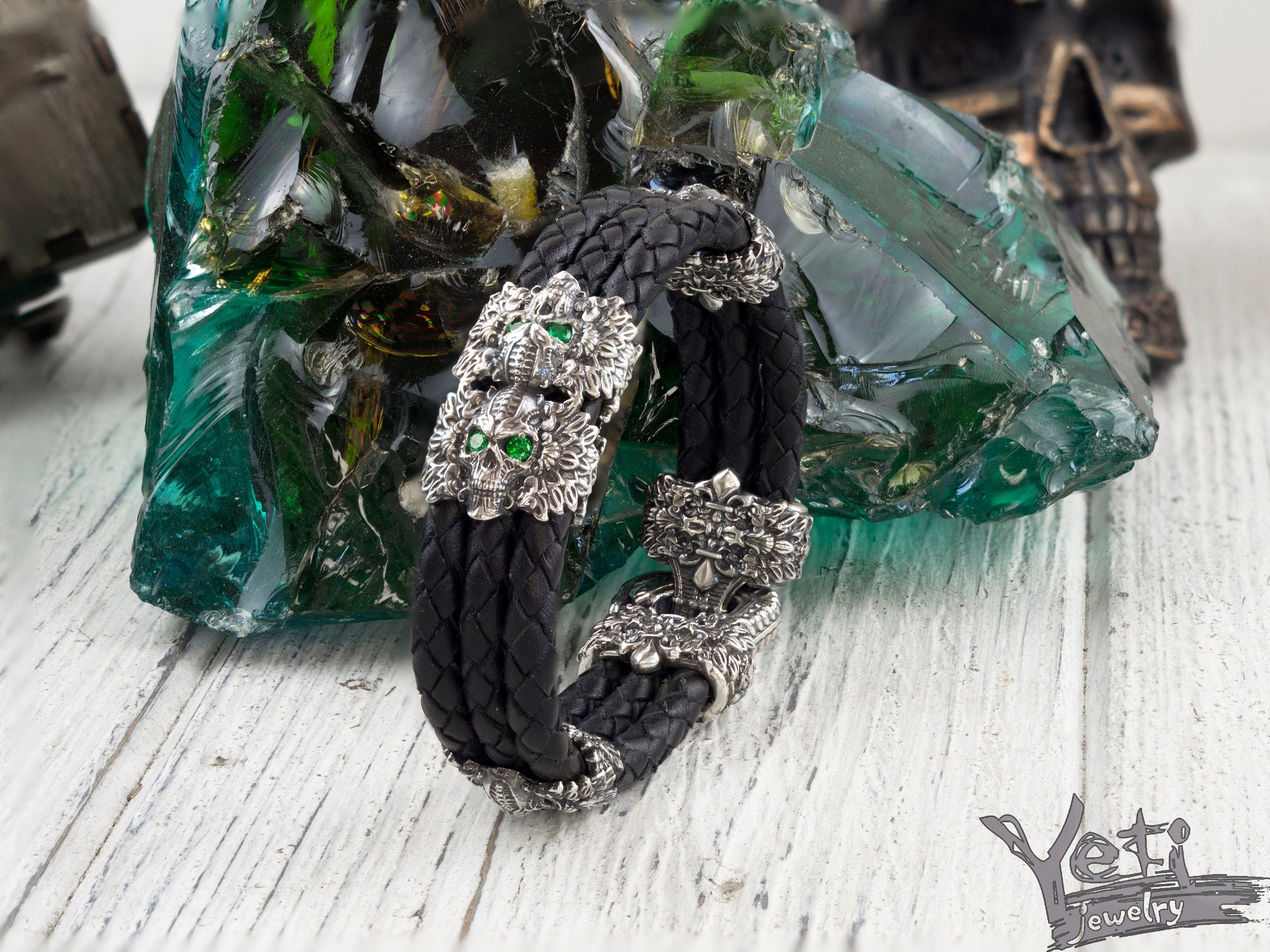Garry braided black leather bracelet with silver feathered skulls and green eyes