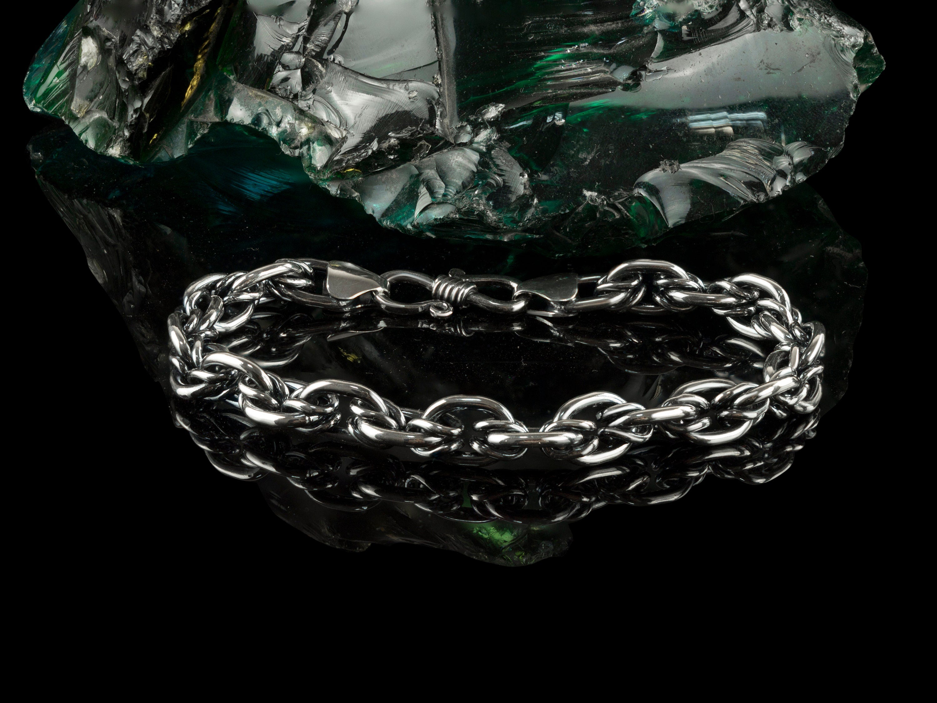 Graf silver bracelet resting on a dark rock, angled view