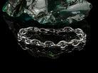 Graf silver bracelet resting on a dark rock, angled view