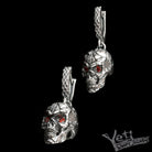 Silver skull dangle earrings with red eyes, angled hanging view