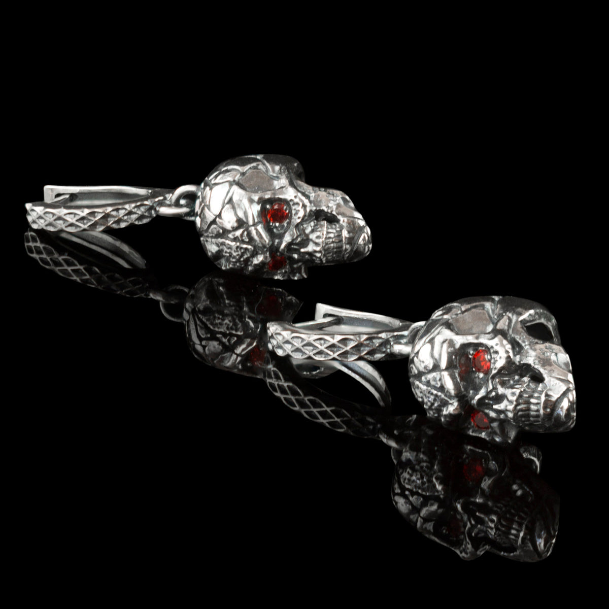 Pair of cracked skull earrings lying on black, side view with leverback hoops