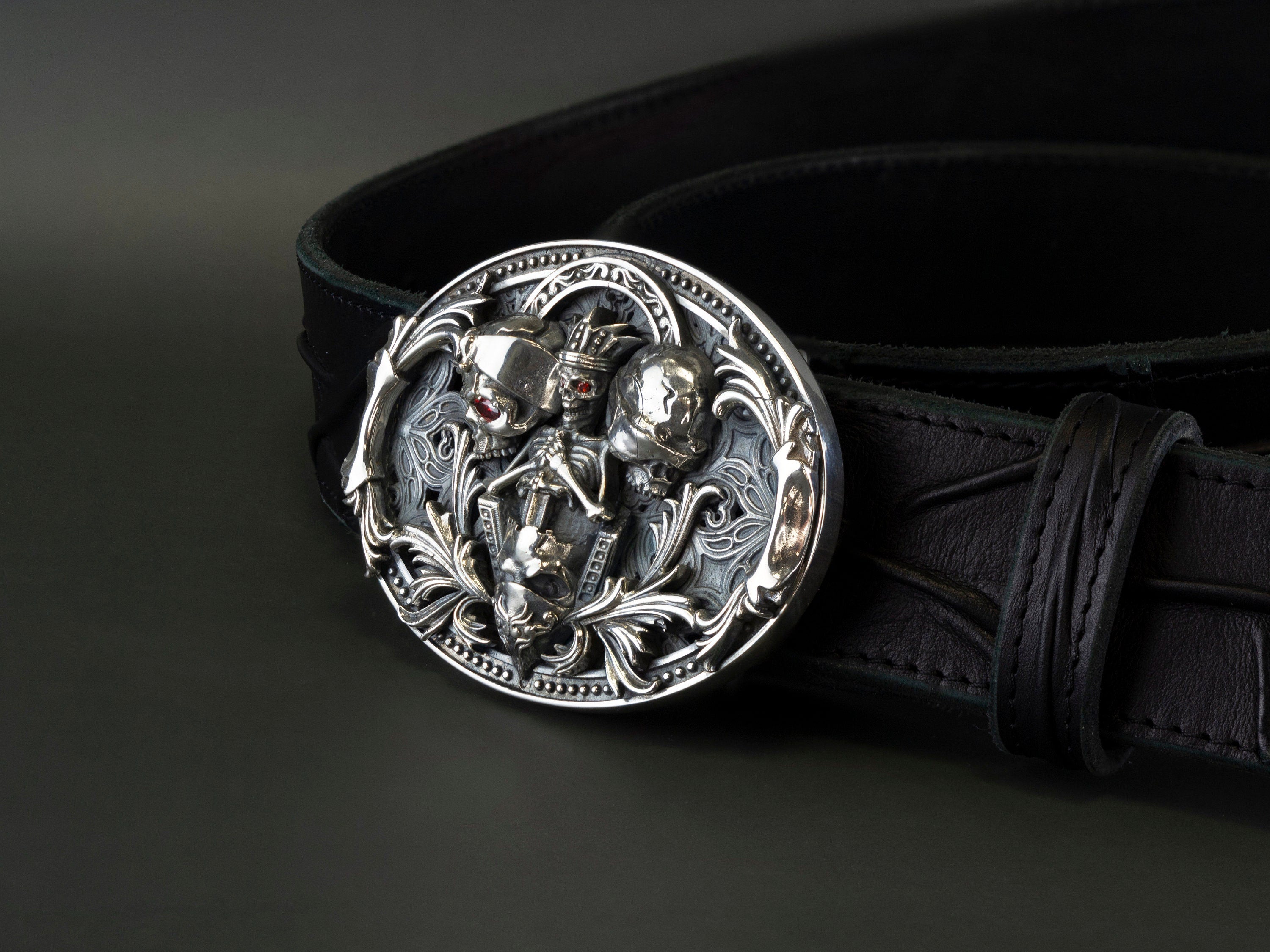Sterling silver skull belt buckle on a black leather belt, angled view