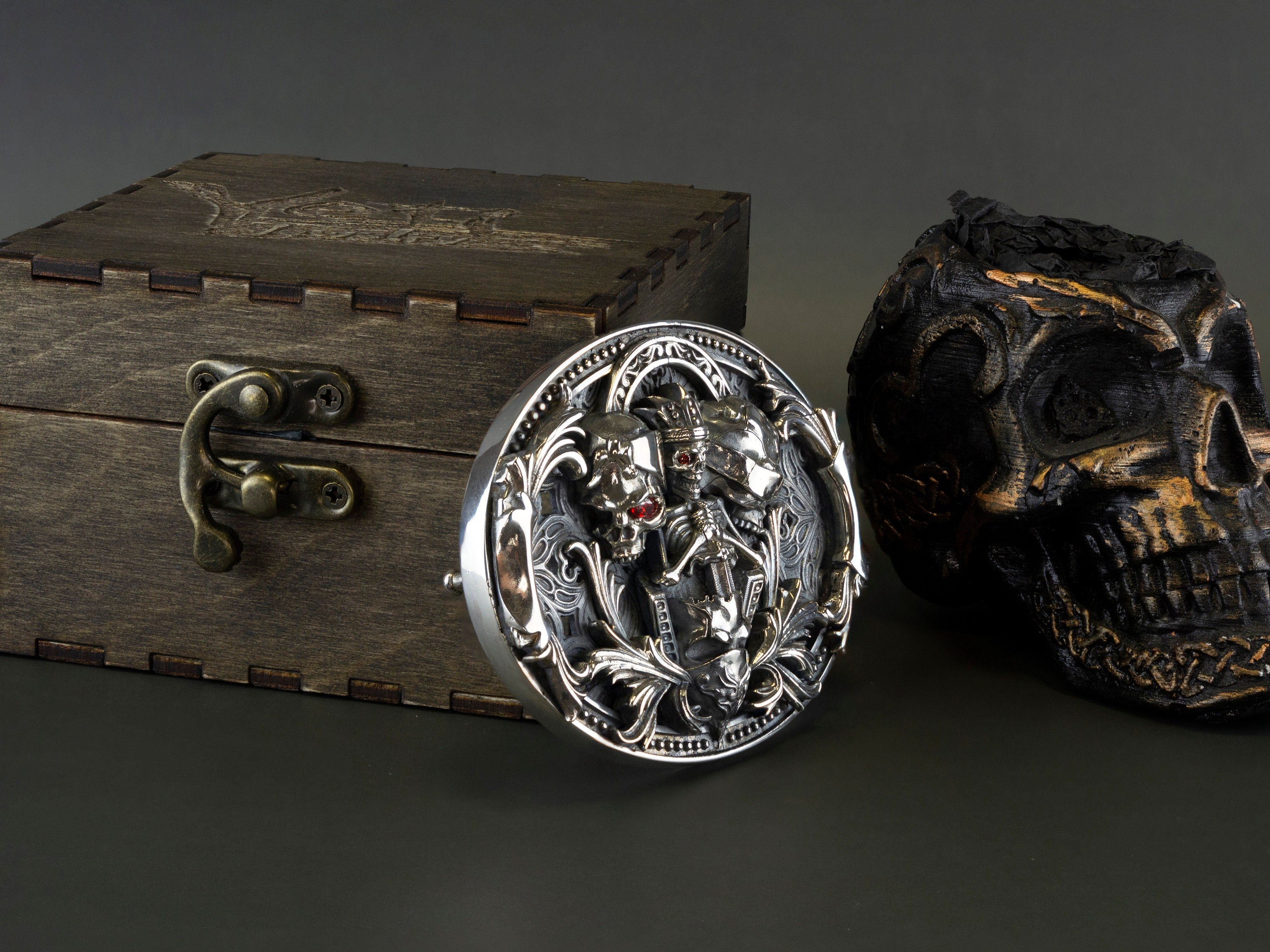 Heavy silver skull buckle standing next to a wooden box, side angle
