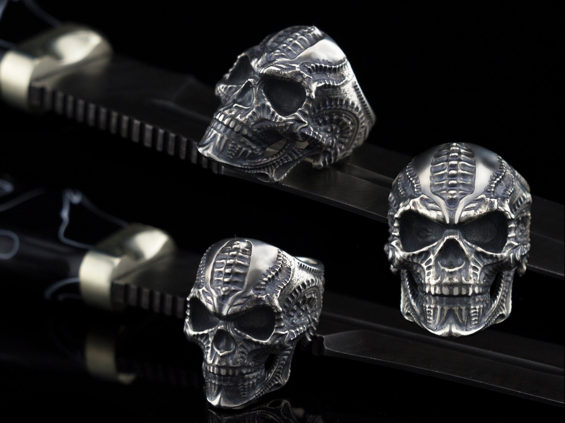 Biomechanical sterling silver skull ring shown from three angles on black background