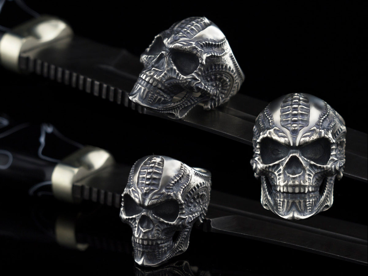 Biomechanical sterling silver skull ring shown from three angles on black background