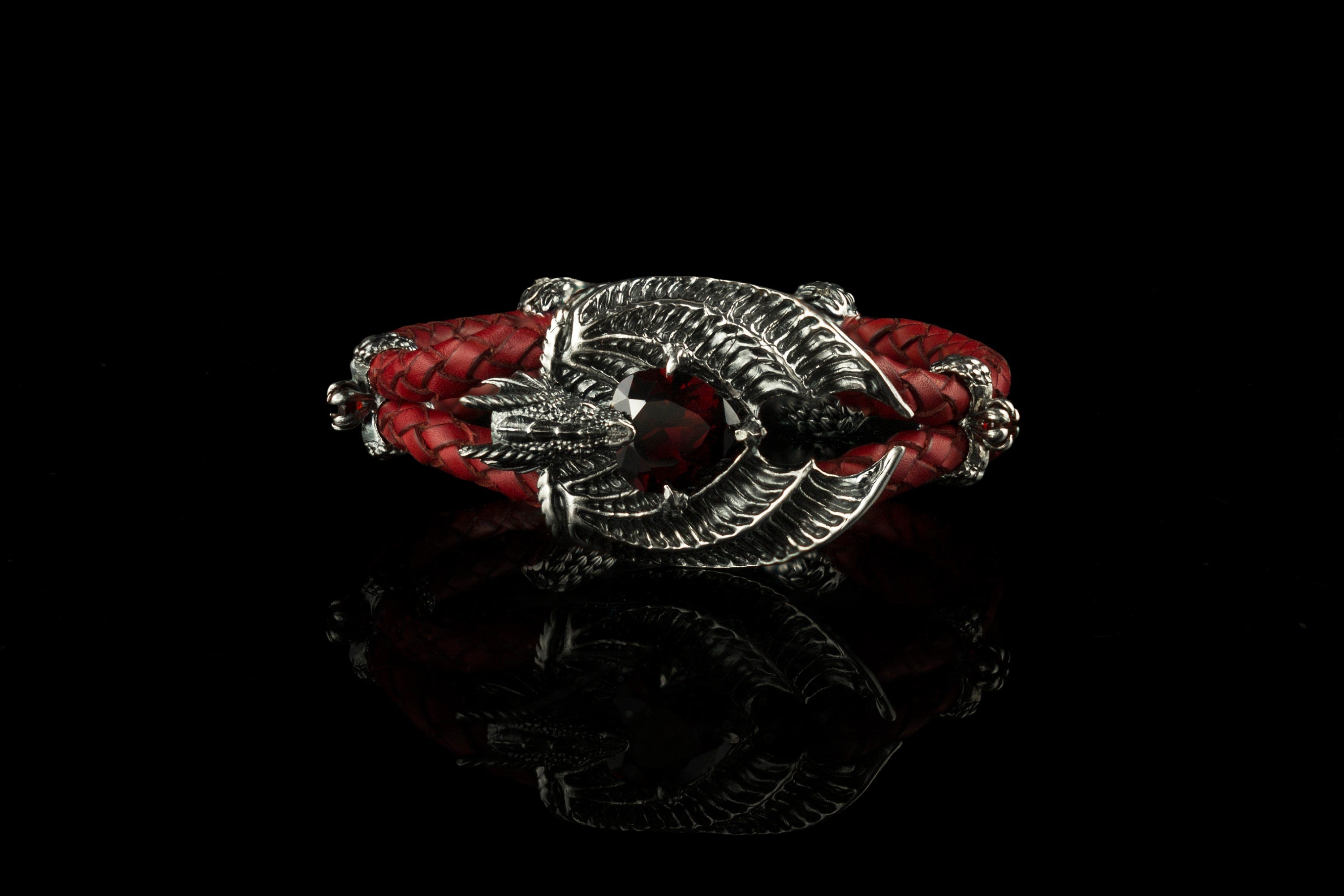 The Dragon Heart bracelet by Yeti Jewelry features an intricate dragon-inspired centerpiece crafted from 925 sterling silver, a red garnet gemstone and a braided red leather cord. The bracelet measures 18 cm long and 26 mm wide, with an approximate weight of 45 grams. Custom lengths and alternative gemstone options are available upon request.