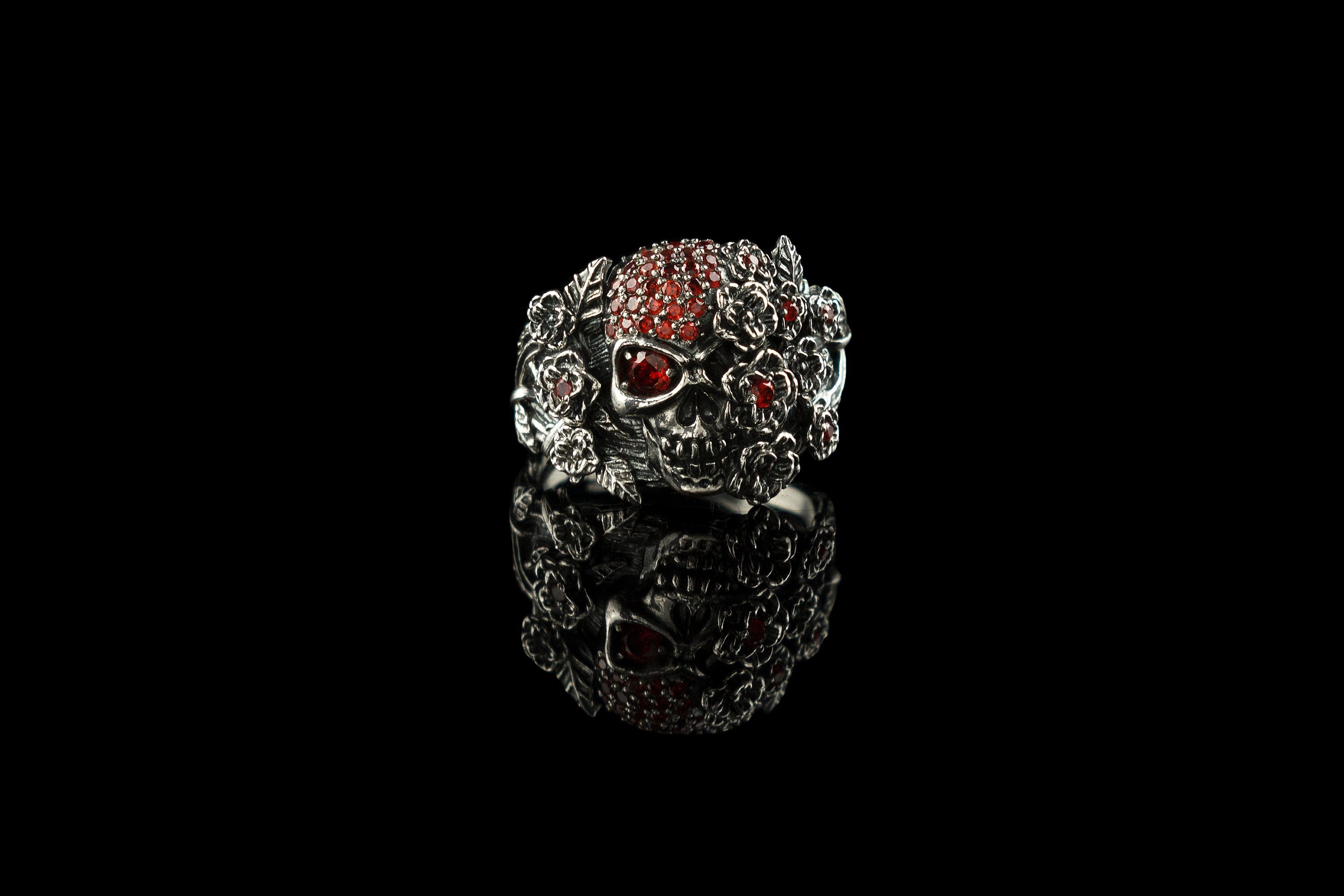Handcrafted 925 sterling silver "Frida" skull ring wrapped in roses with sparkling crimson red cubic zirconia pave on a dark background
