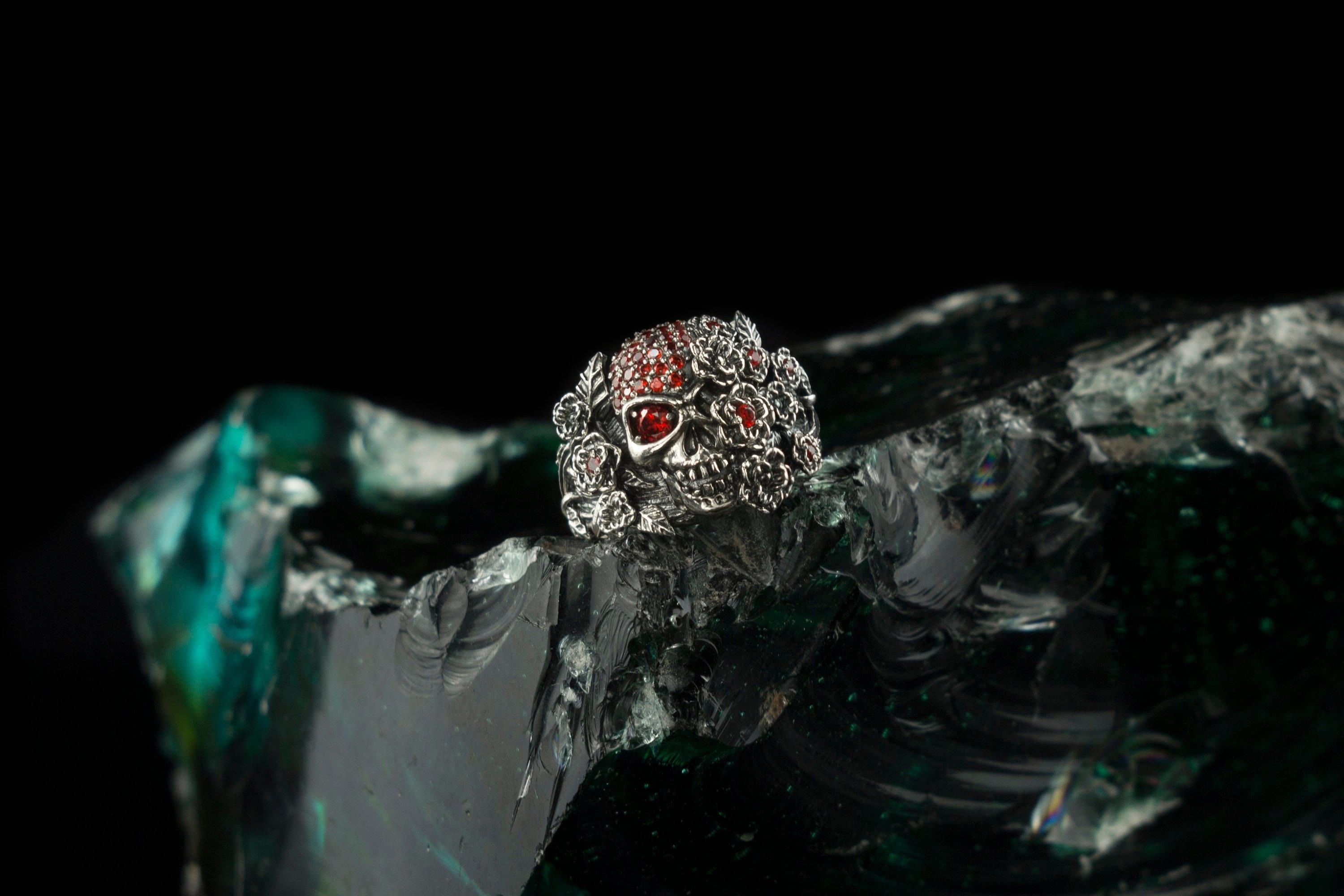 Handcrafted 925 sterling silver "Frida" skull ring wrapped in roses with sparkling crimson red cubic zirconia pave on a dark background