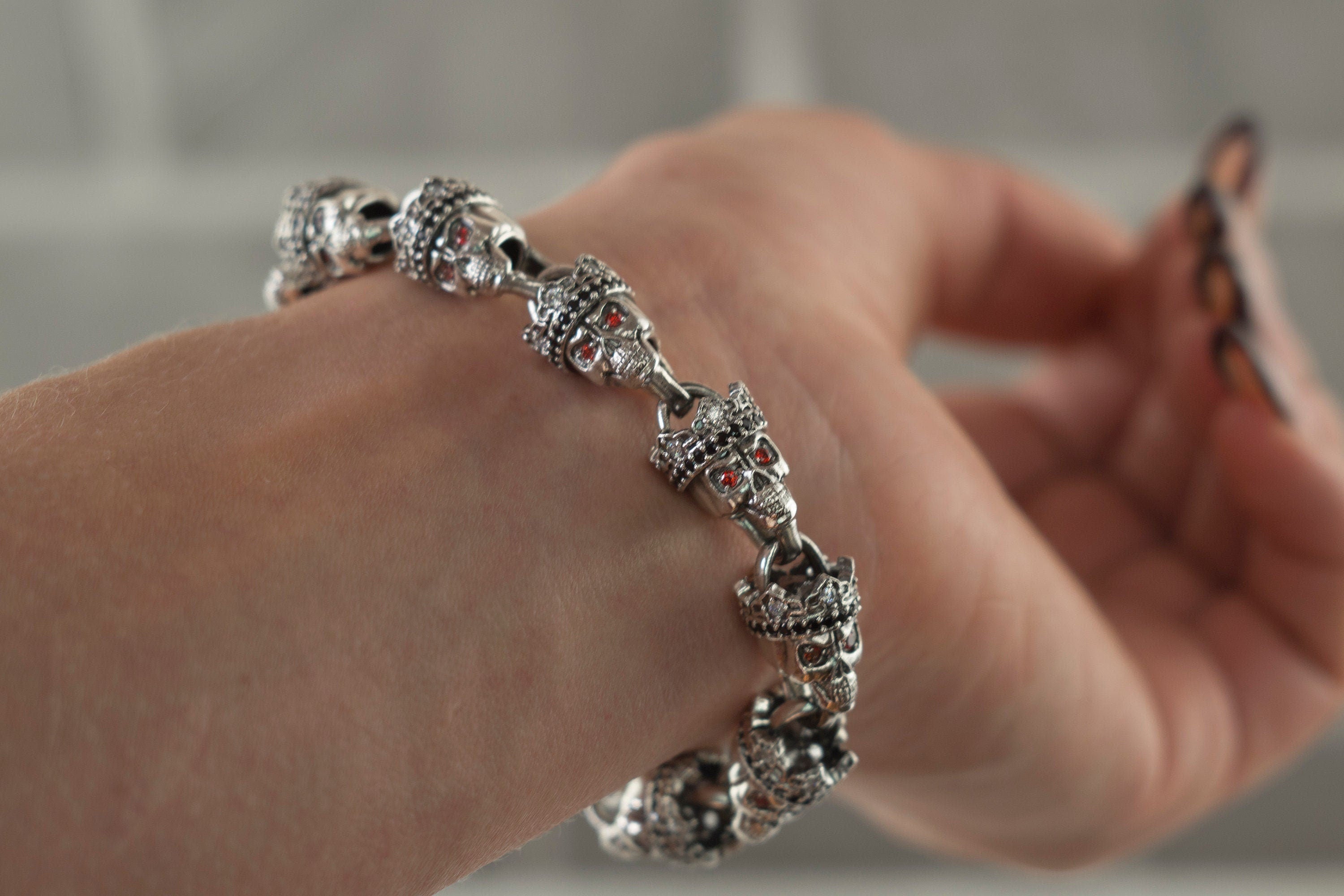 Santa Muerte bracelet in 925 sterling silver featuring linked crowned skulls and red stone accents by Yeti Jewelry