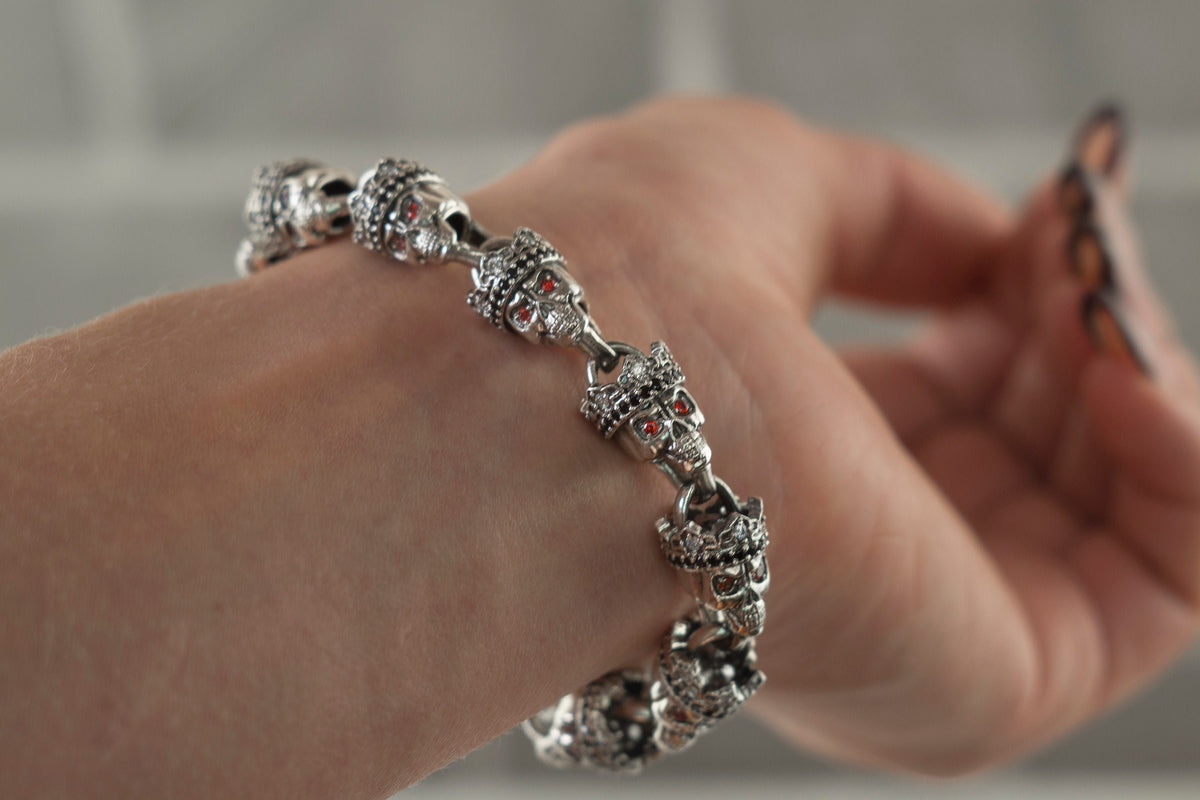 Santa Muerte bracelet in 925 sterling silver featuring linked crowned skulls and red stone accents by Yeti Jewelry