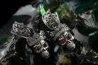 Close-up of Santa Muerte-inspired sterling silver skull earrings showing detailed crowns and red cubic zirconia eyes