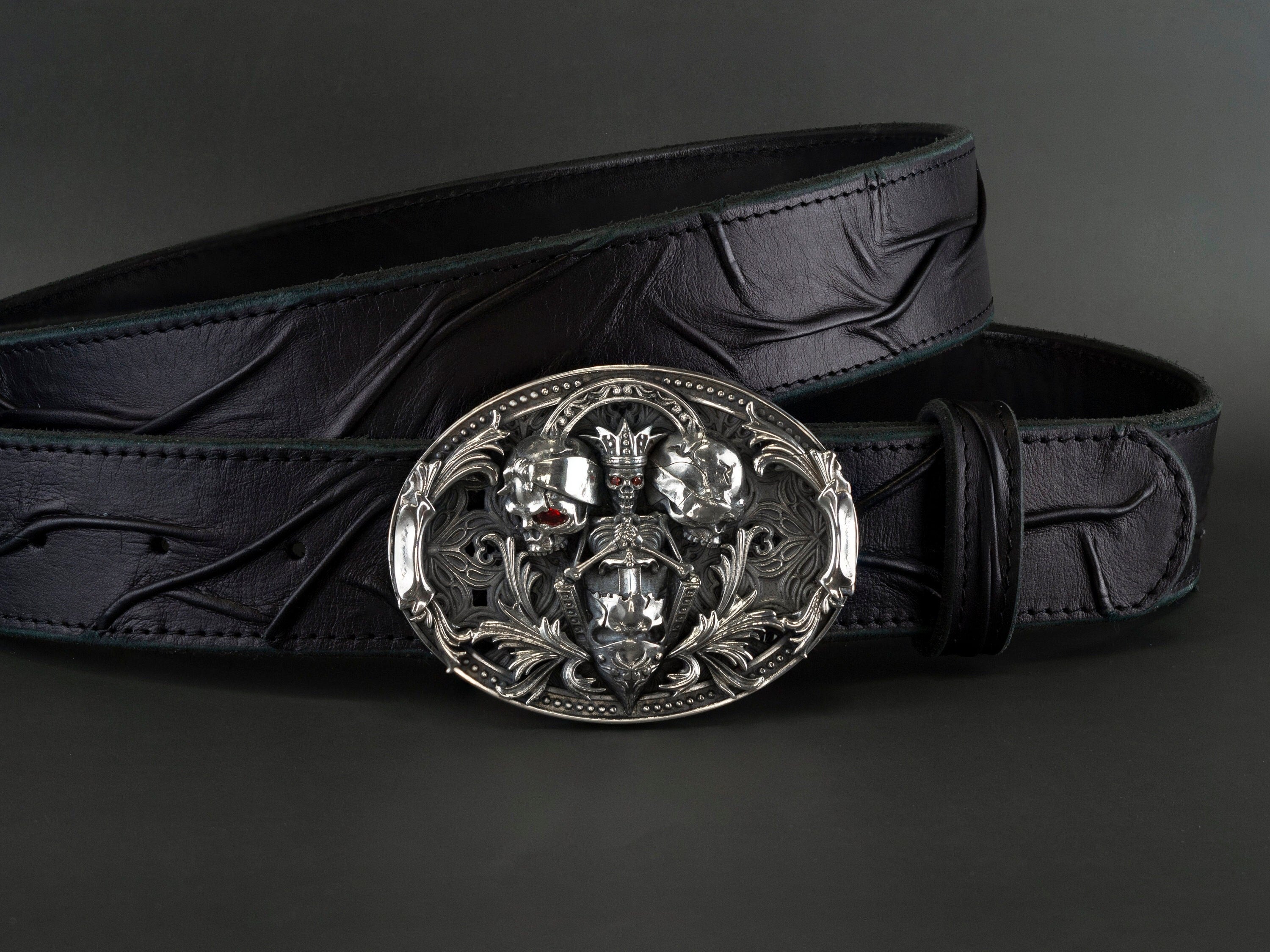 Hear Nothing See Nothing Say Nothing belt buckle in sterling silver 925 featuring sculpted skulls, ornate scrollwork, and red cubic zirconia accents on a black leather belt.