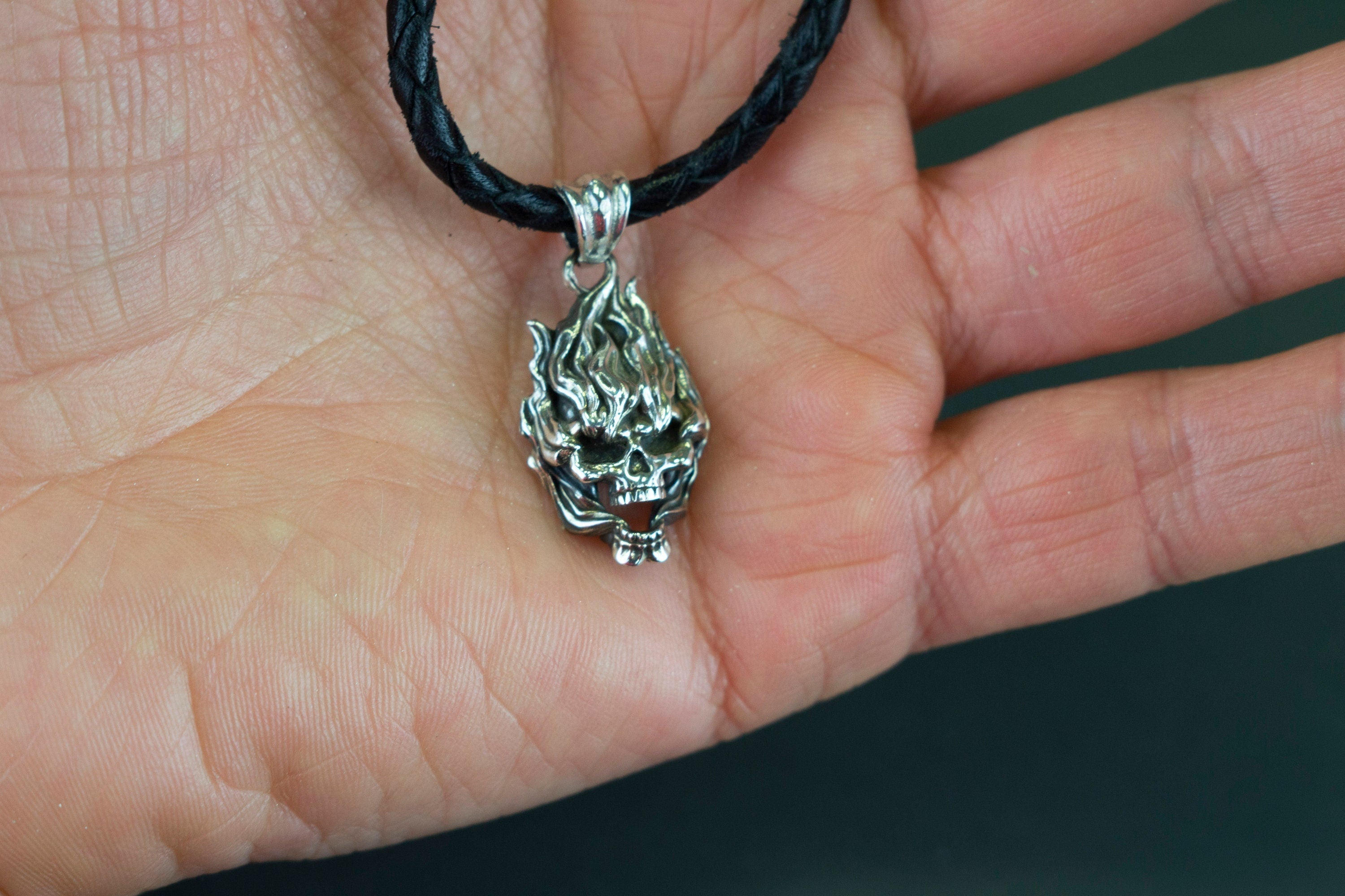 Emeric small 925 sterling silver skull pendant with sculpted flame-like details and polished highlights, displayed on a black cord.