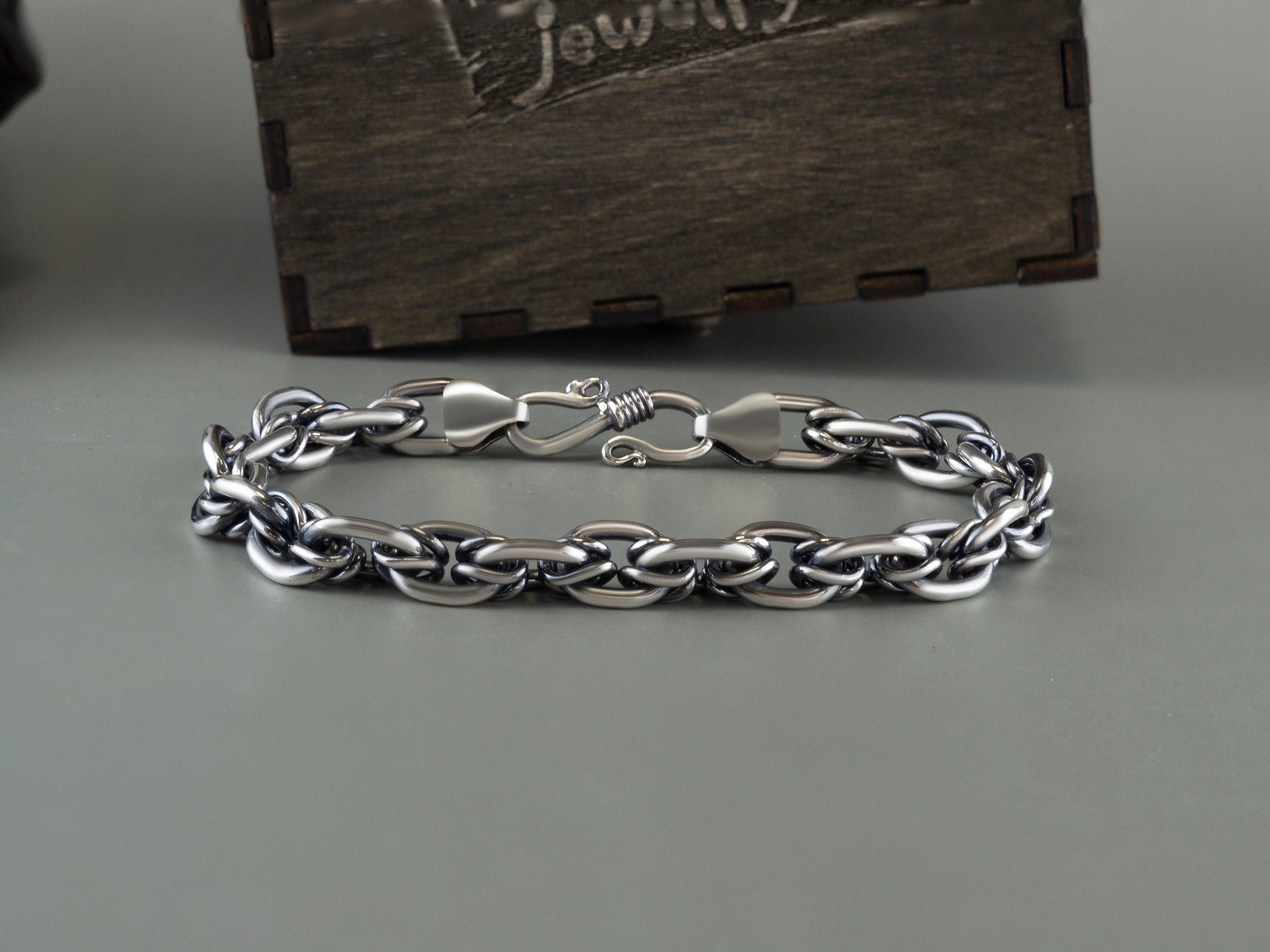 Heavy 925 sterling silver chain bracelet with polished interlocking links and a decorative clasp, displayed on a gray background beside a Yeti Jewelry wooden box.