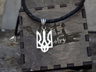Ukrainian Tryzub pendant in polished 925 sterling silver displayed on a black braided leather cord against a branded wooden jewelry box.