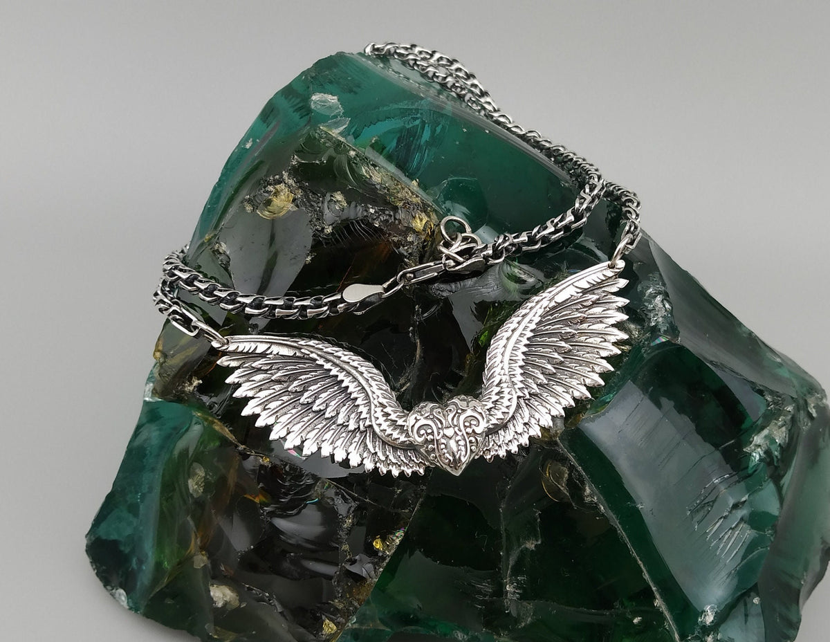 Angelisa sterling silver angel wings necklace with intricately sculpted feathers and an ornate central detail, displayed on a dark green decorative stone.