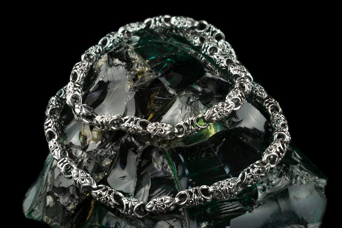Ornate sterling silver chain draped in loops, showing oxidized link pattern