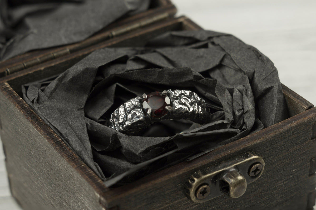 Mons Igneus textured silver ring with red garnet resting in black paper