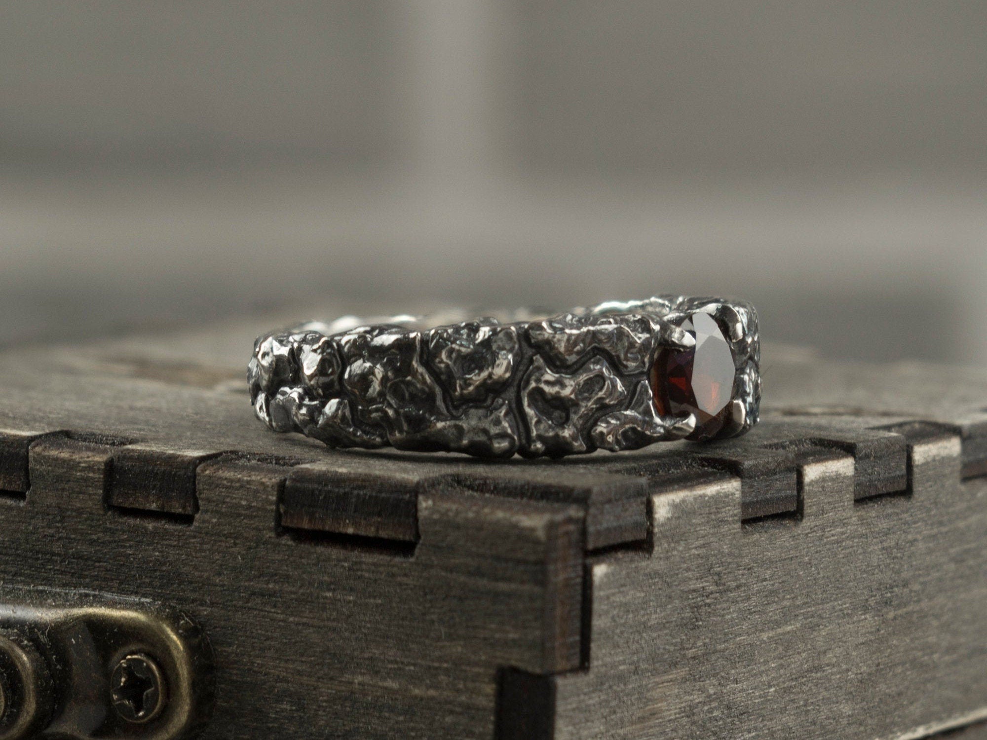 Textured silver garnet ring standing on a box, three-quarter view
