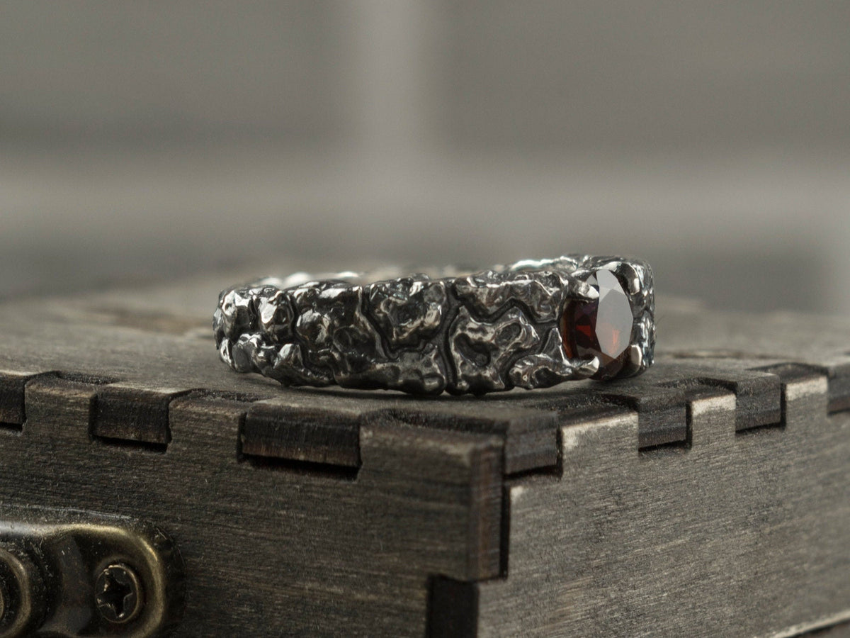 Textured silver garnet ring standing on a box, three-quarter view