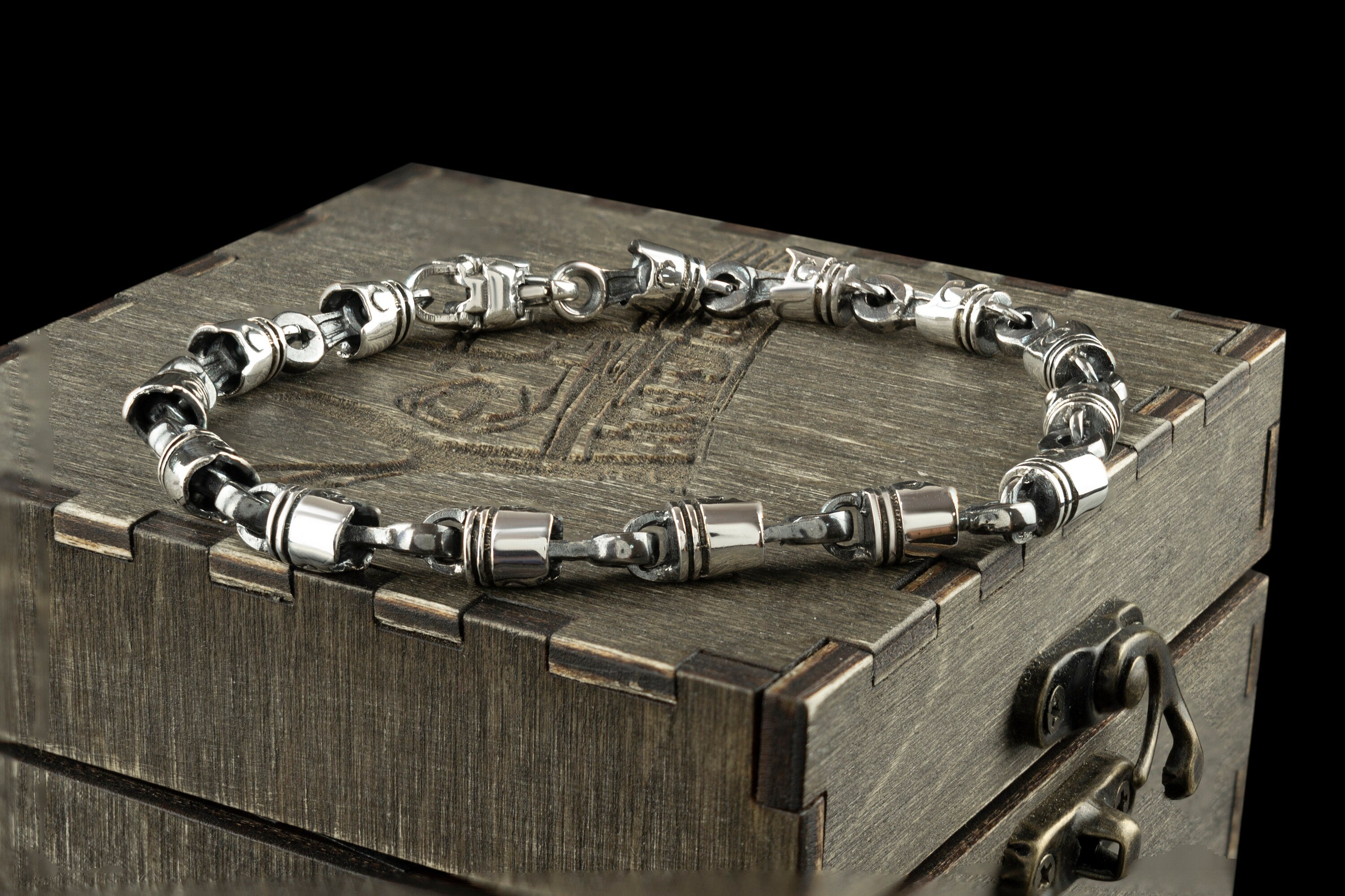 Silver piston link bracelet lying on the lid of an engraved wooden gift box