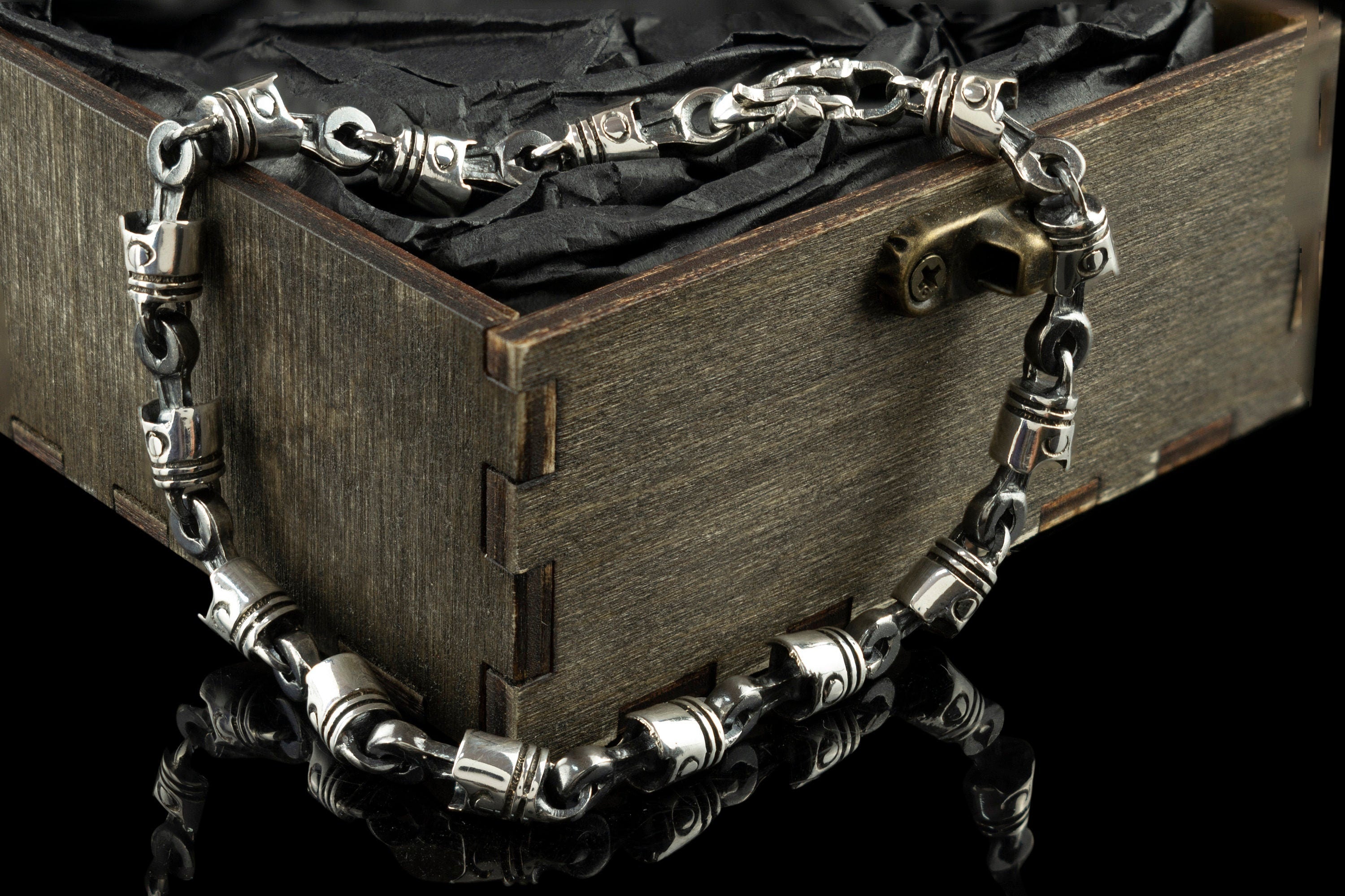 Piston and rod sterling silver biker bracelet draped over a wooden box