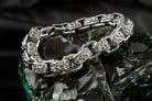 Rory ornate silver biker bracelet laid in a loop, polished edges and dark textured ornament