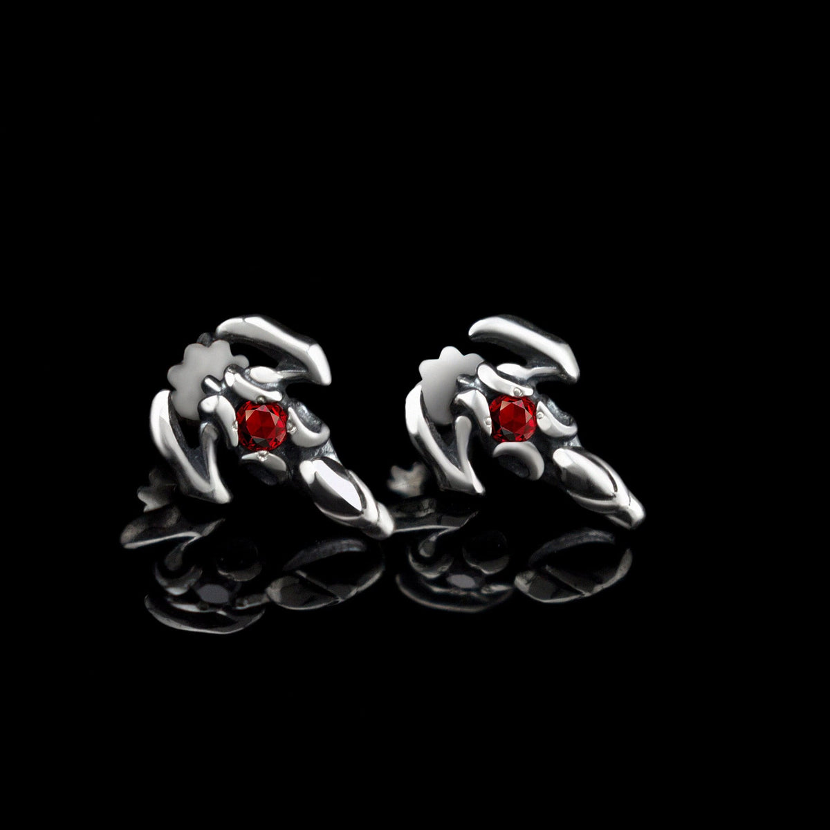 Pair of sterling silver scorpion stud earrings with red cubic zirconia on a black background
