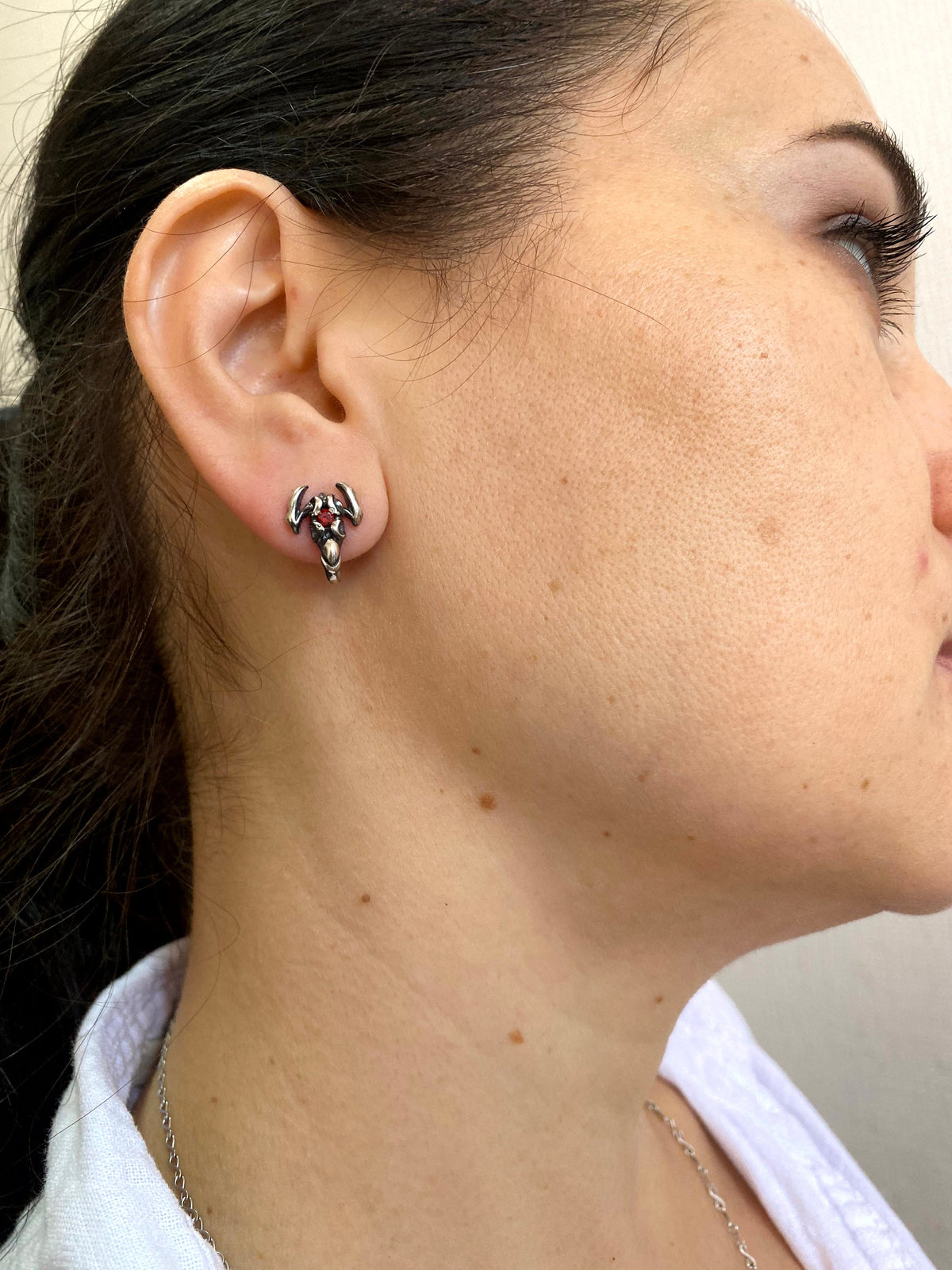 Woman wearing a silver scorpion stud earring with red stone, side profile