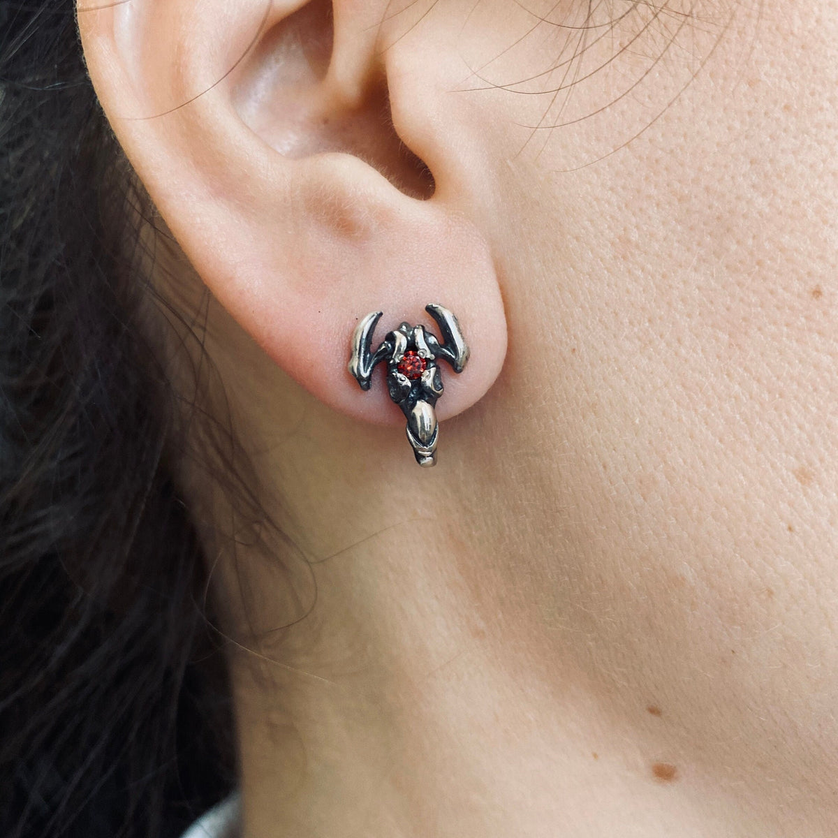 Scorpion sterling silver stud earring with red stone worn on the ear, close-up