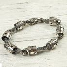 Silver piston and rod bracelet laid out on a white wooden surface