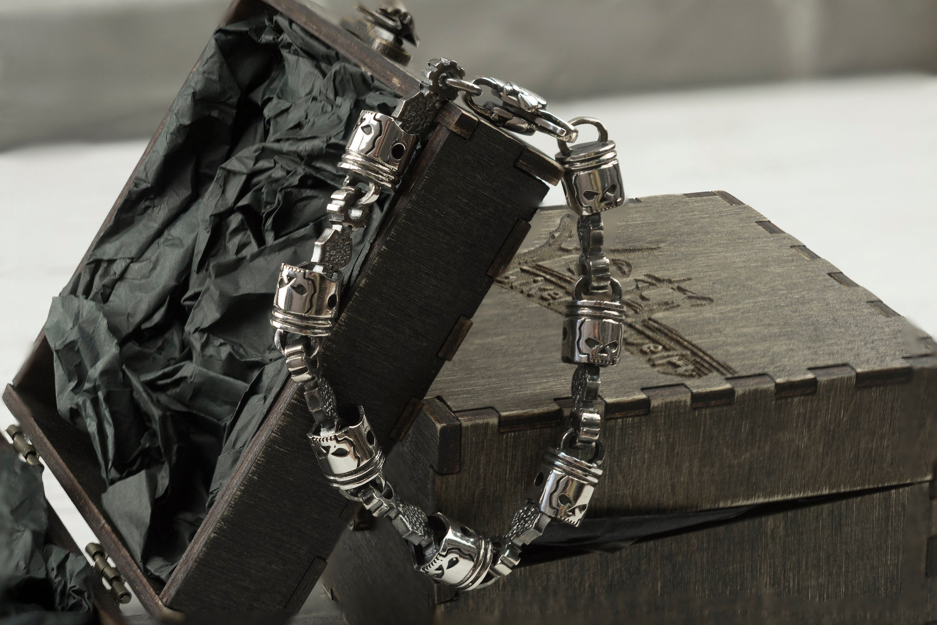 Skull piston heavy silver biker bracelet draped over a wooden box