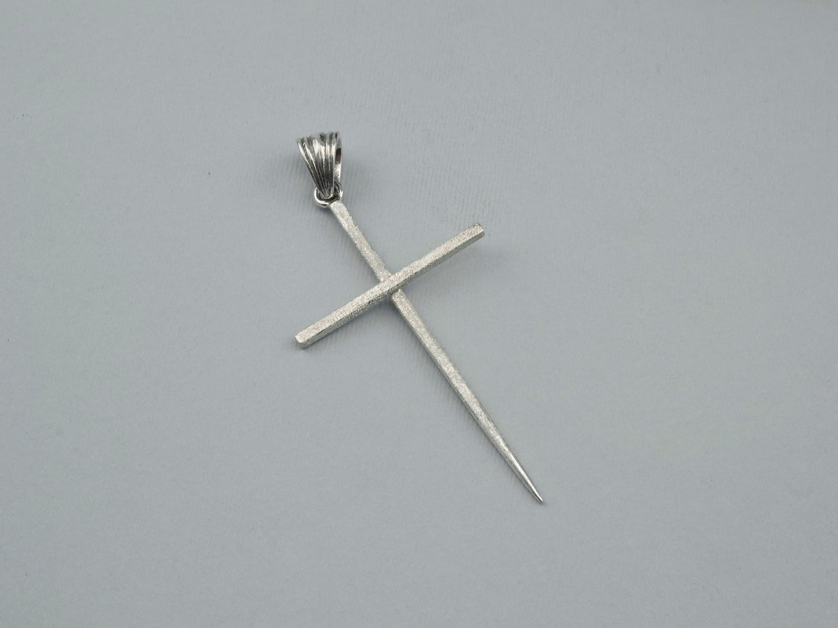 Long sterling silver spike cross pendant with ribbed bail on a light background