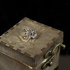 Tiny Frida sterling silver floral skull pendant with red stone eyes, on box top