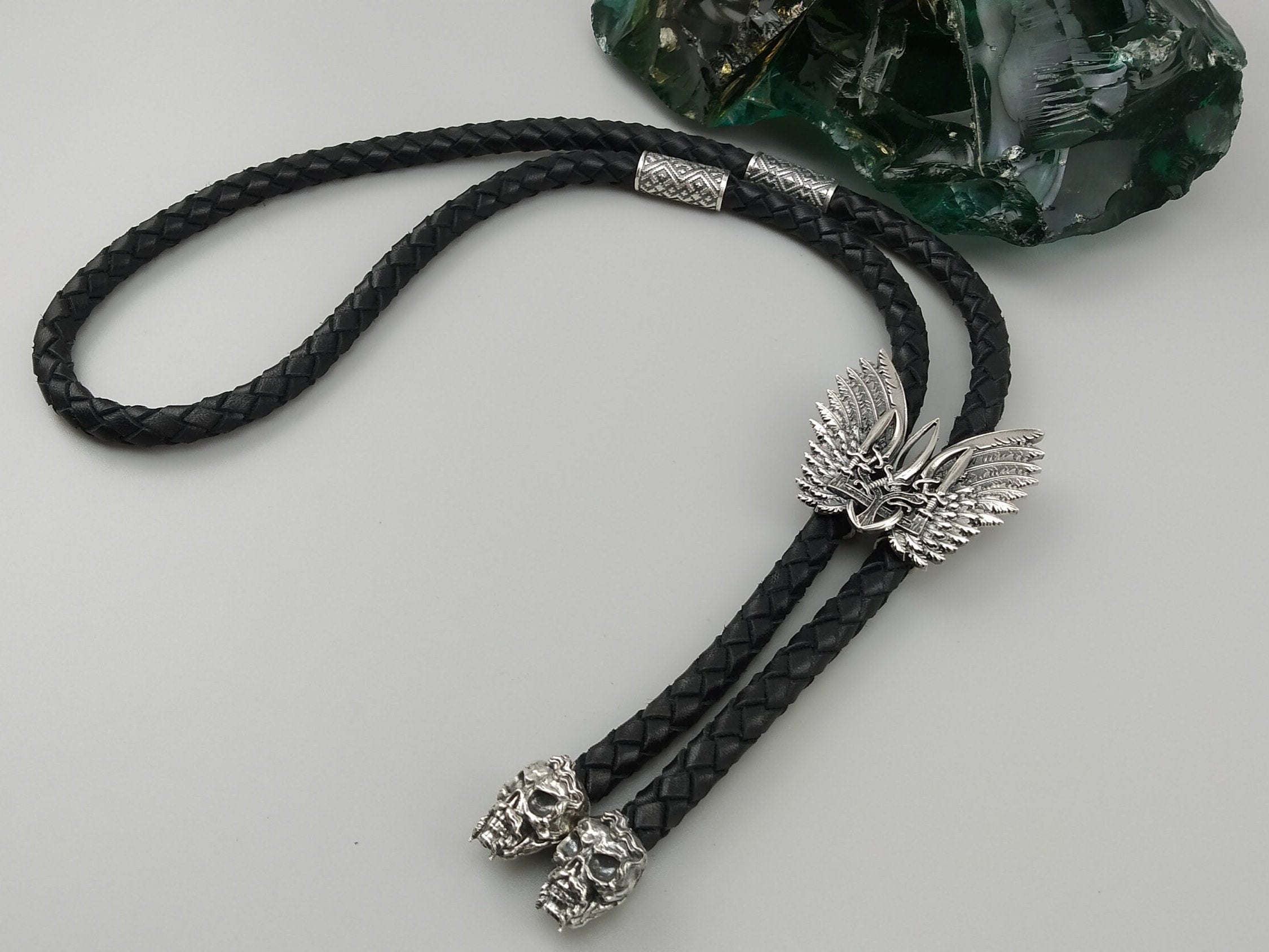 Tryzub bolo tie with silver wings and braided leather cord, full view on gray