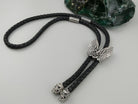 Tryzub bolo tie with silver wings and braided leather cord, full view on gray