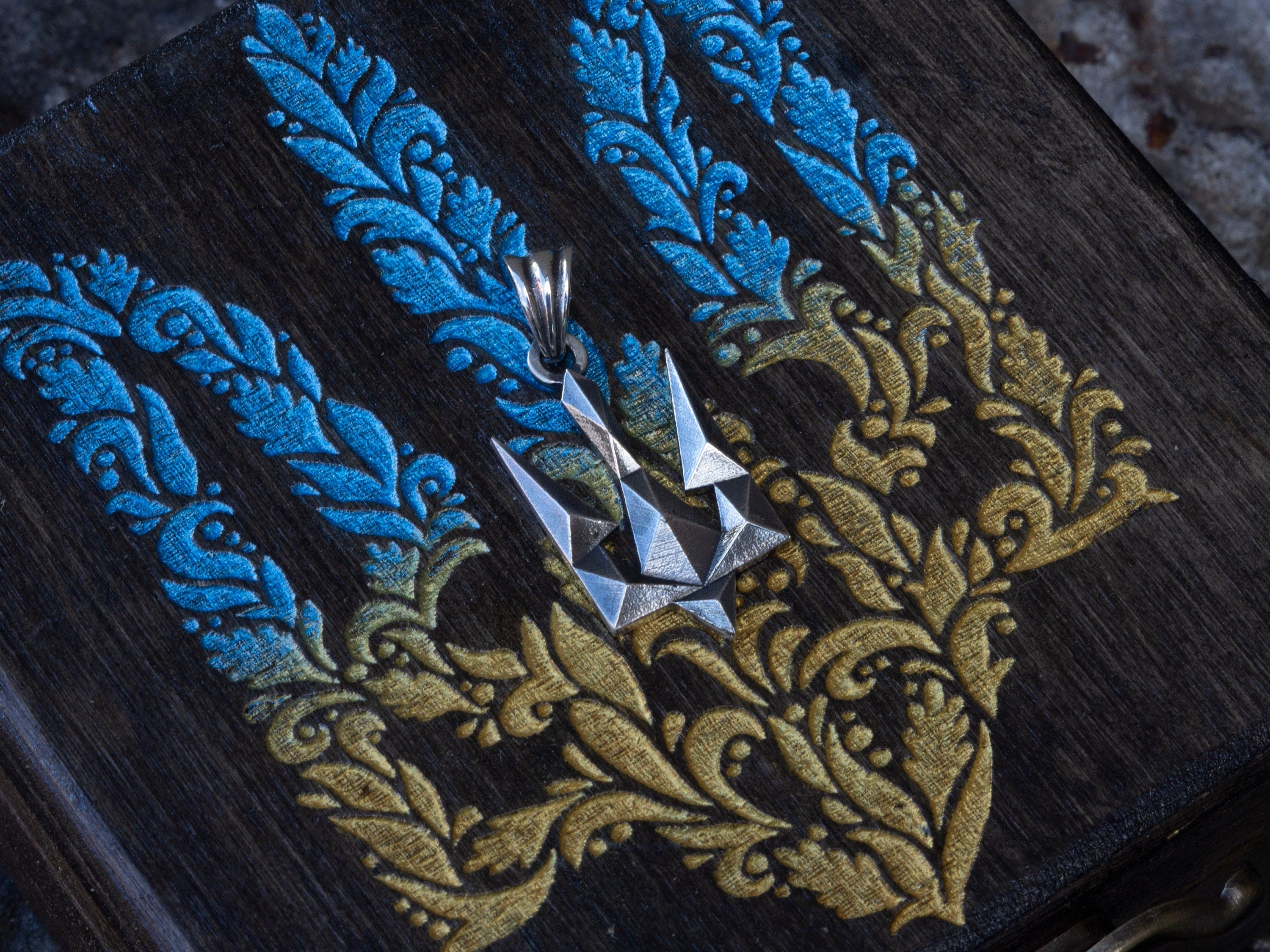 Silver trident pendant on blue and yellow embroidered fabric