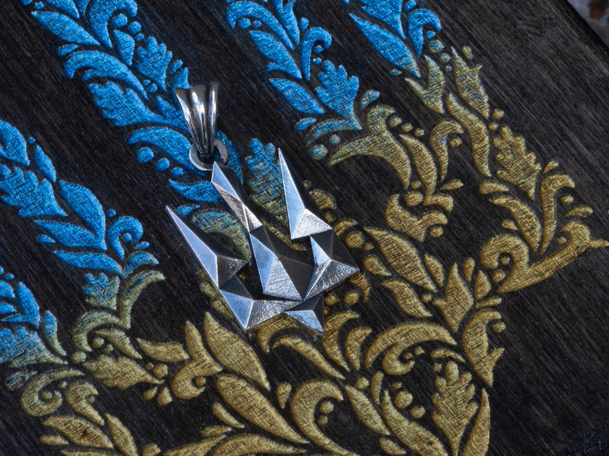 Tryzub silver pendant on blue and yellow fabric, angled view