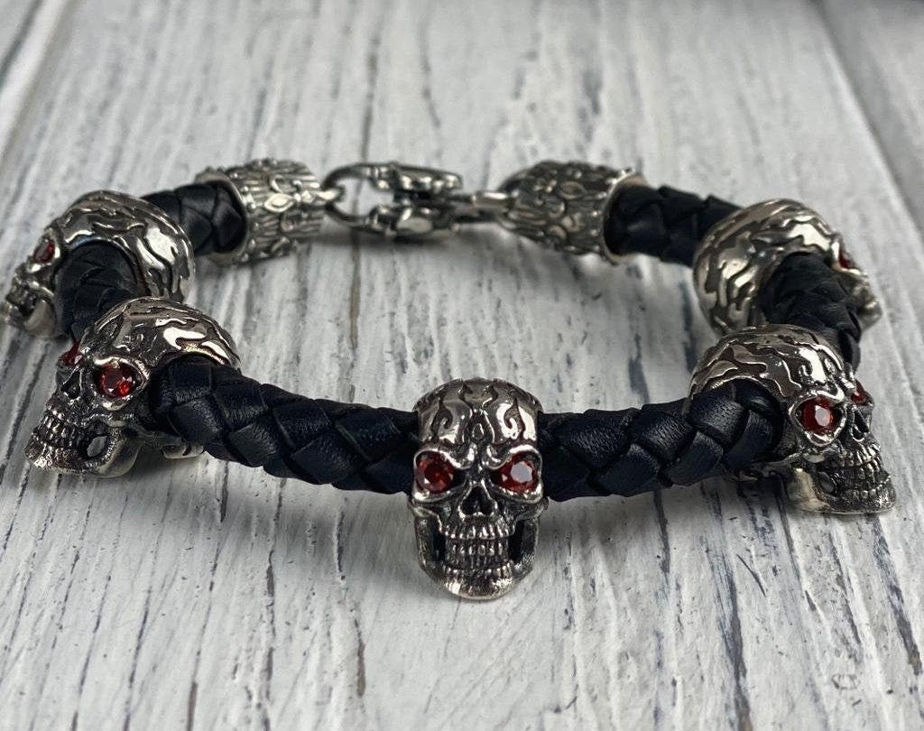 Wild skull braided leather biker bracelet with silver skulls and red eyes on white wood