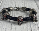Wild skull braided leather biker bracelet with silver skulls and red eyes on white wood