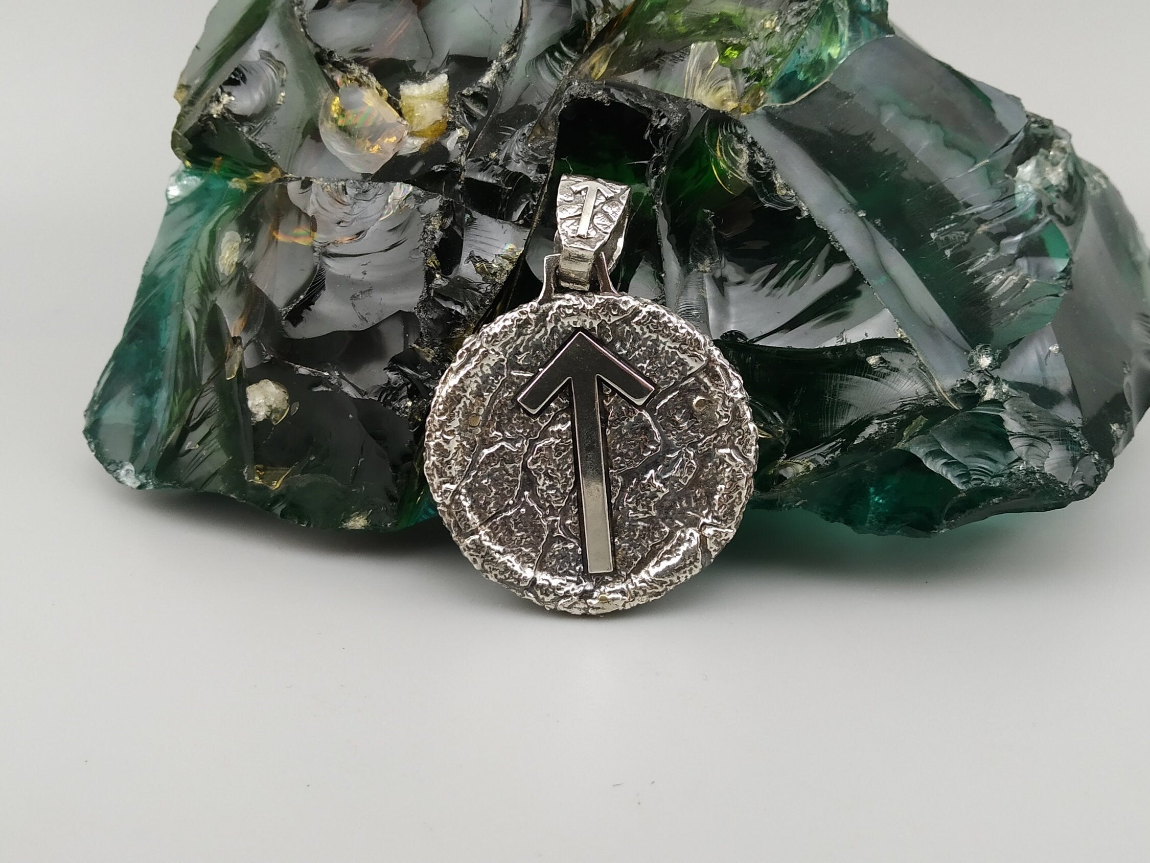 Round silver pendant with Tiwaz rune arrow on a textured oxidized background