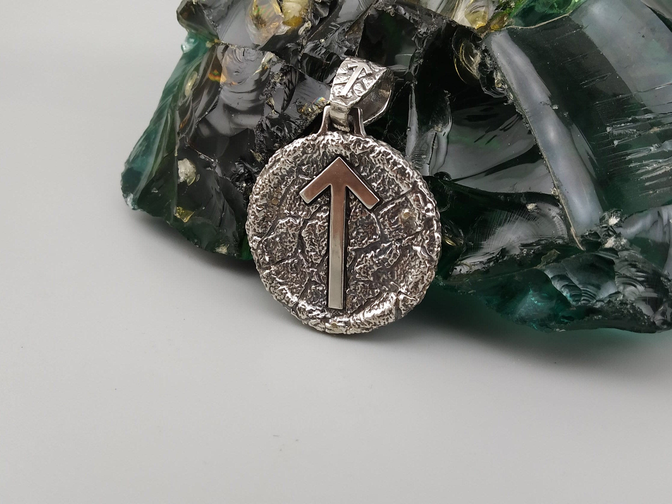Close-up of the Tiwaz rune arrow on a round oxidized silver pendant